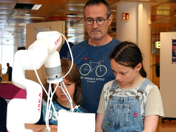 Bernd Semar mit seinen Kindern Ruven und Liv beobachten den Roboterarm beim Materialschnitt. Fotos, O-Ton: Harald Denckmann